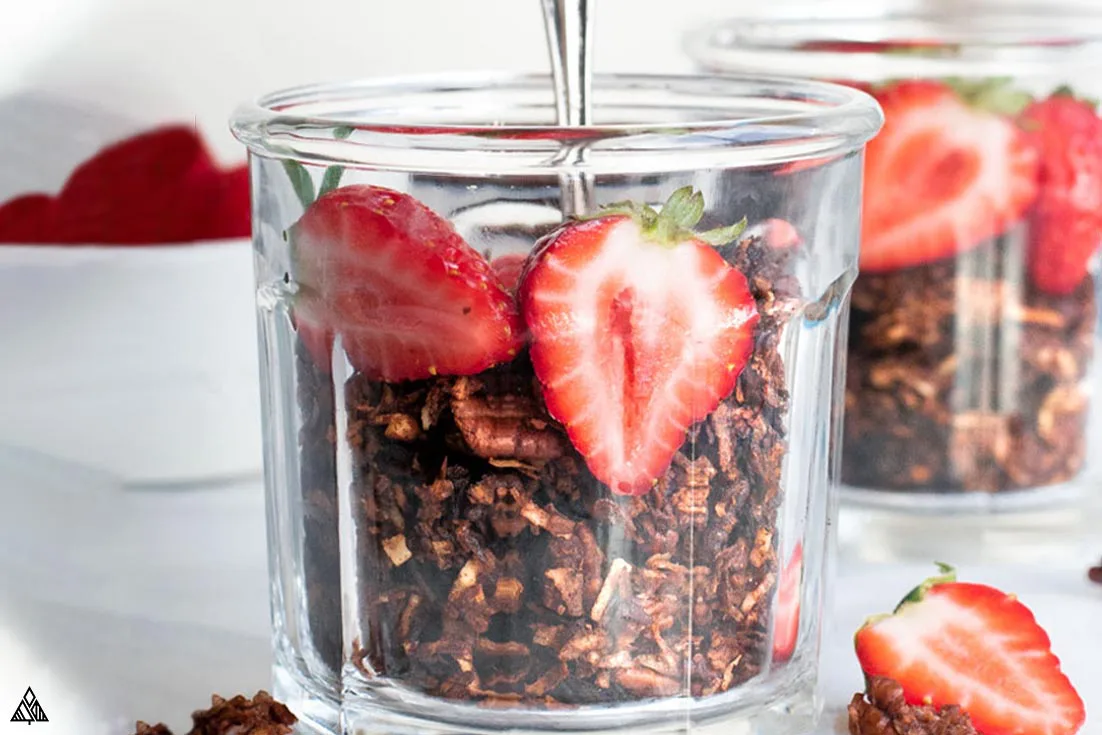 Side view of low carb chocolate granola in a glass with sliced strawberries