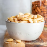 Blanched almonds in a cup with a jar of almonds with skin at the background