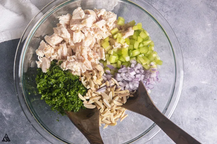 chicken salad ingredients in a large bowl with spoons--an easy keto chicken recipe