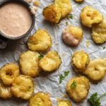 Low carb fried pickles on a parchment paper with a dip on the side