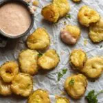 Low carb fried pickles on a parchment paper with a dip on the side