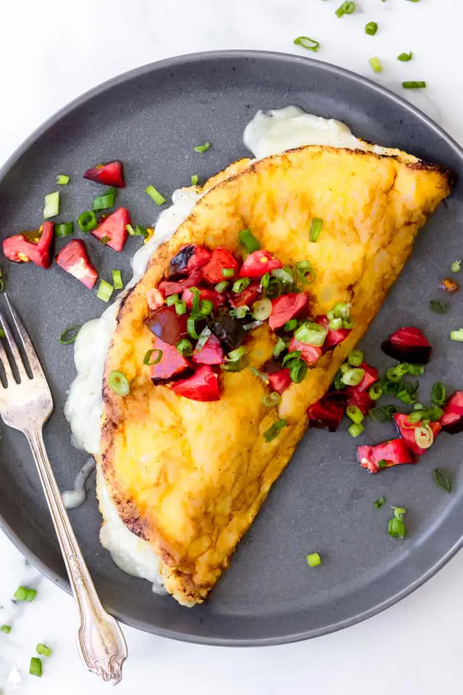 soufflé omelette on a plate with tomatoes and green onions