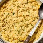 cheesy cauliflower rice recipes in a pan with a spoon and chives