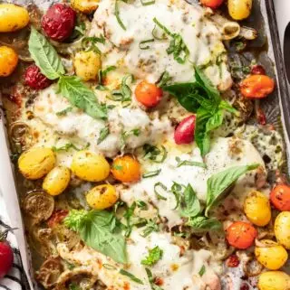 baked pesto chicken on a baking sheet with tomatoes and basil