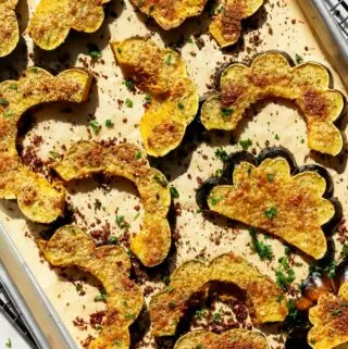 roasted acorn squash recipe on a baking sheet with parmesan and fresh herbs on top