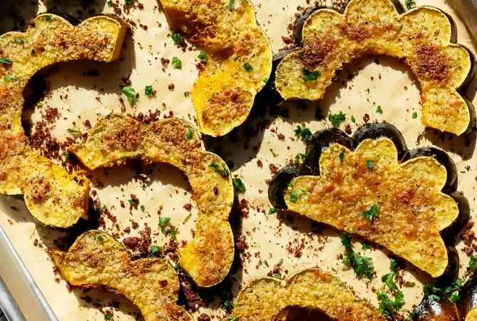 roasted acorn squash recipe on a baking sheet with parmesan and fresh herbs on top