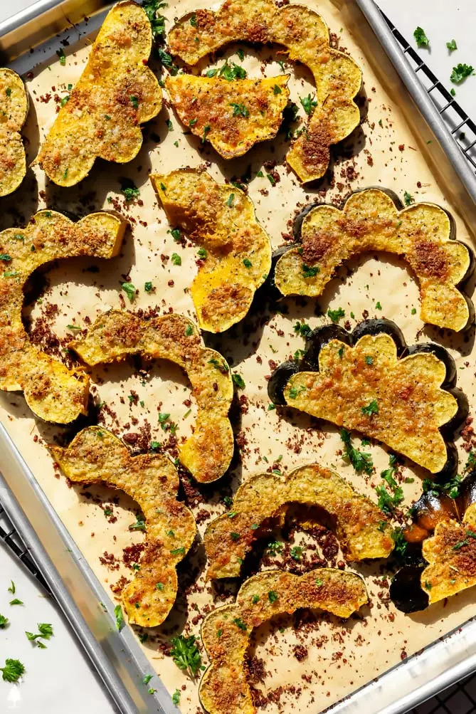 roasted squash recipe on a baking sheet with parmesan and fresh herbs on top