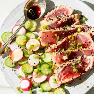 seared ahi tuna recipe on a plate with sauce, green onions, radish and cucumber salad, and seasoning.