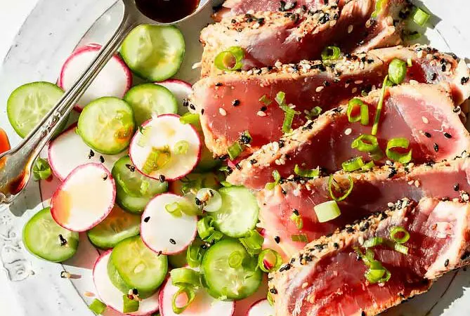 seared ahi tuna recipe on a plate with sauce, green onions, radish and cucumber salad, and seasoning.