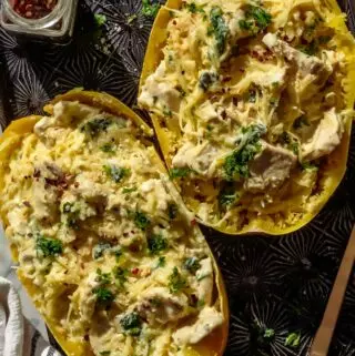 spaghetti squash alfredo in spaghetti squash boats, on a baking dish with red pepper flakes