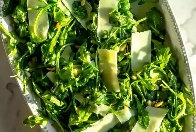 arugula salad in a platter with parmesan cheese on top