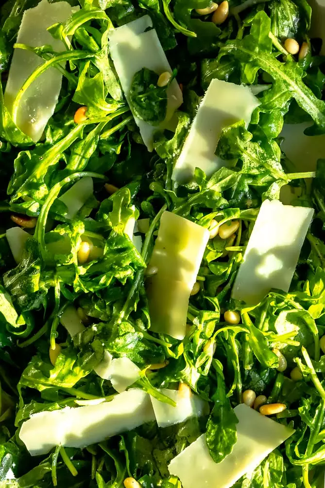 arugula salad dressing over a rocket salad with large pieces of parmesan