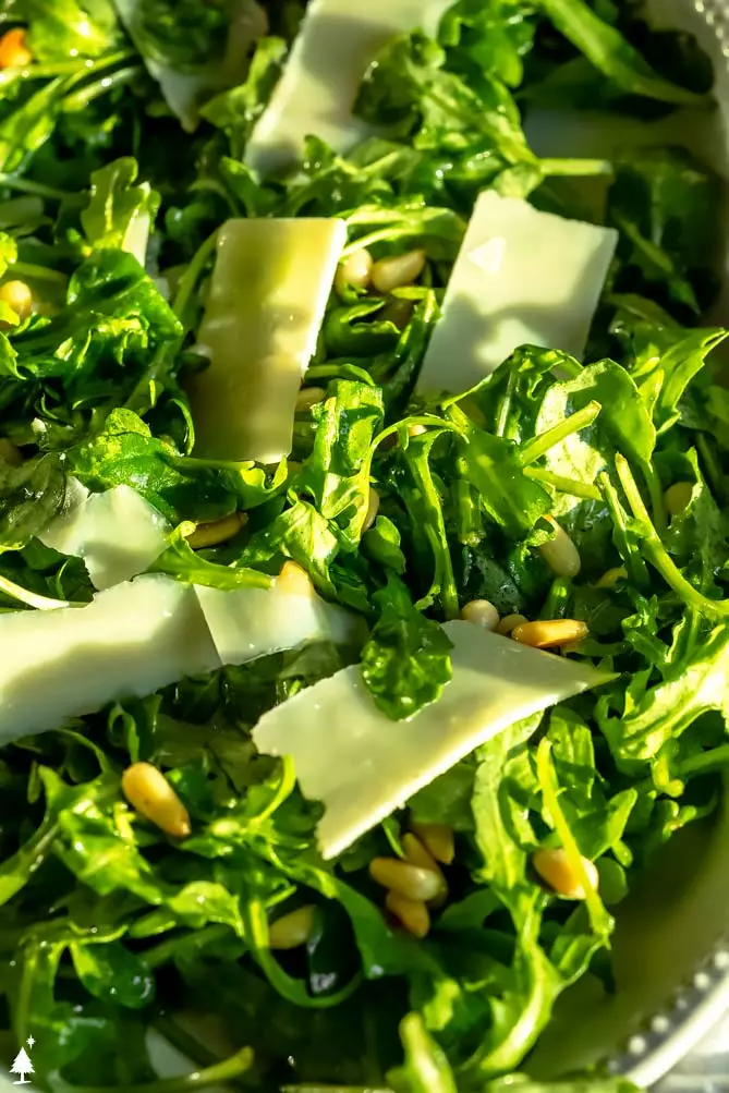 close up of arugula salad on a platter with parmesan cheese on top