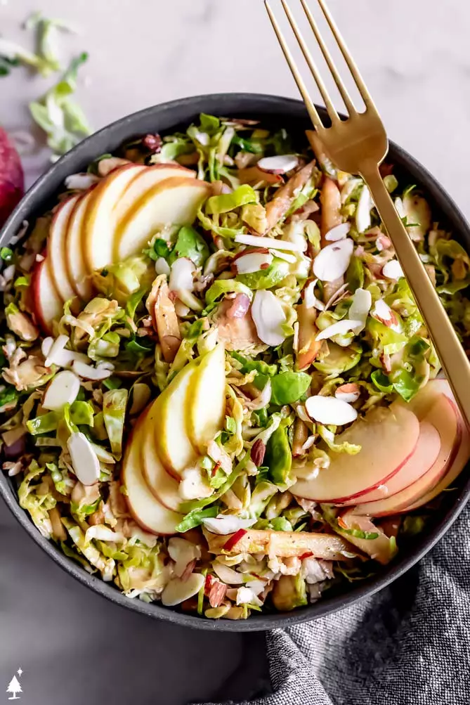 shredded brussel sprouts salad in a bowl with apple and a fork