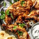 Tandoori chicken recipe on a baking sheet with cilantro, red onions, naan, and yogurt sauce