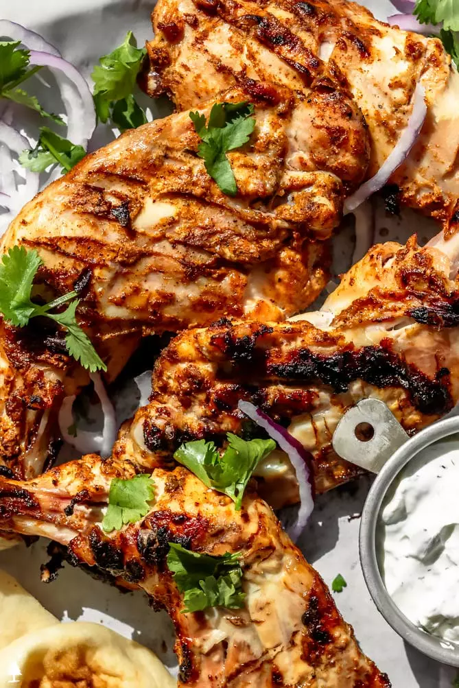 tandoori chicken in oven on a baking sheet with yogurt sauce and cilantro