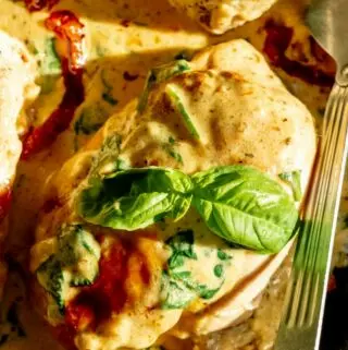 close up of creamy tuscan chicken with basil and a large serving spoon