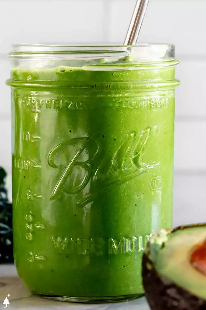 close up of kale smoothie recipe with an avocado and kale in the background