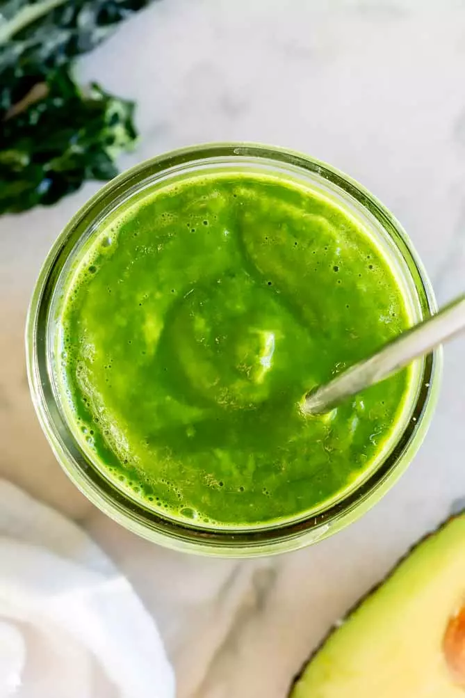 kale protein smoothie recipe in a cup, overhead with an avocado and kale
