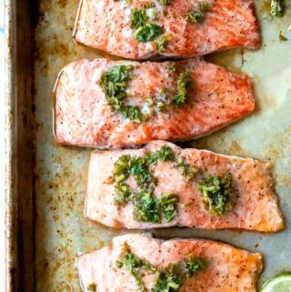 salmon chimichurri on a baking sheet with extra sauce on the side