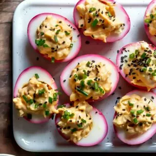 beet pickled deviled eggs on a platter with chives and seeds