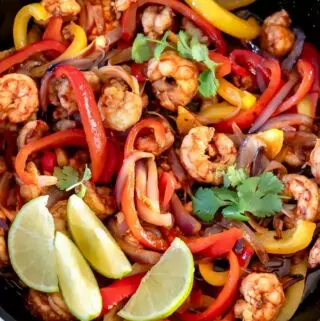 shrimp fajitas recipe in a skillet with peppers, onions, cilantro and limes